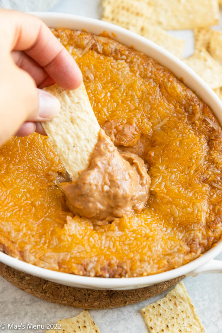A hand dipping a dip into the refried bean dip with cream cheese.