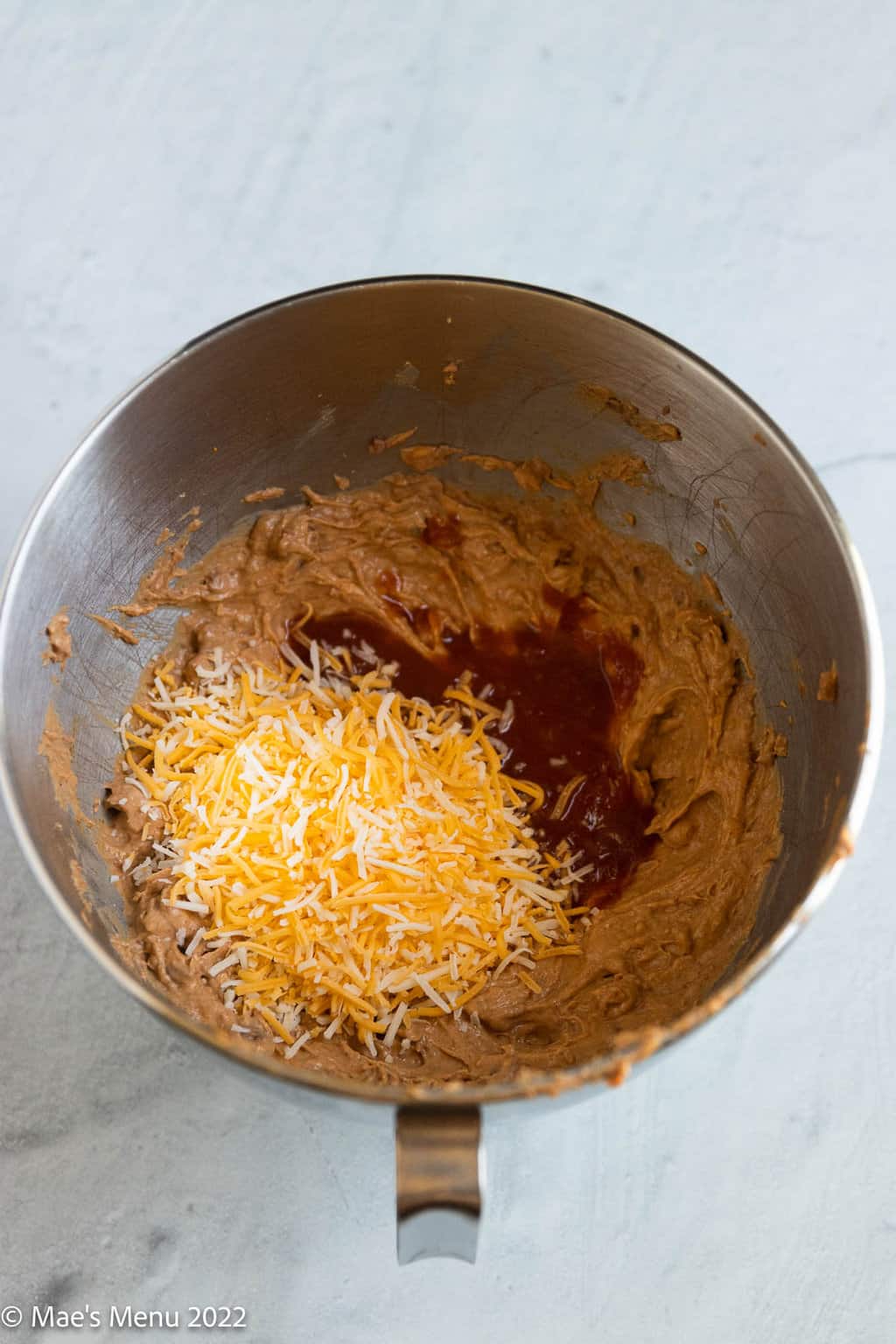 A mixing bowl of refried beans mix, salsa, and shredded cheese.
