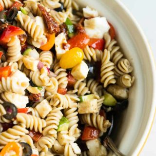 A ceramic bowl of balsamic pasta salad with a silver serving spoon.