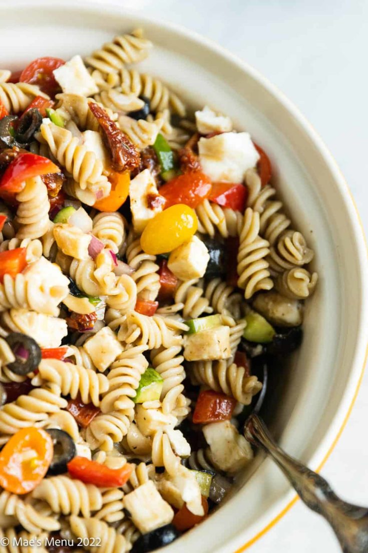 A ceramic bowl of balsamic pasta salad with a silver serving spoon.
