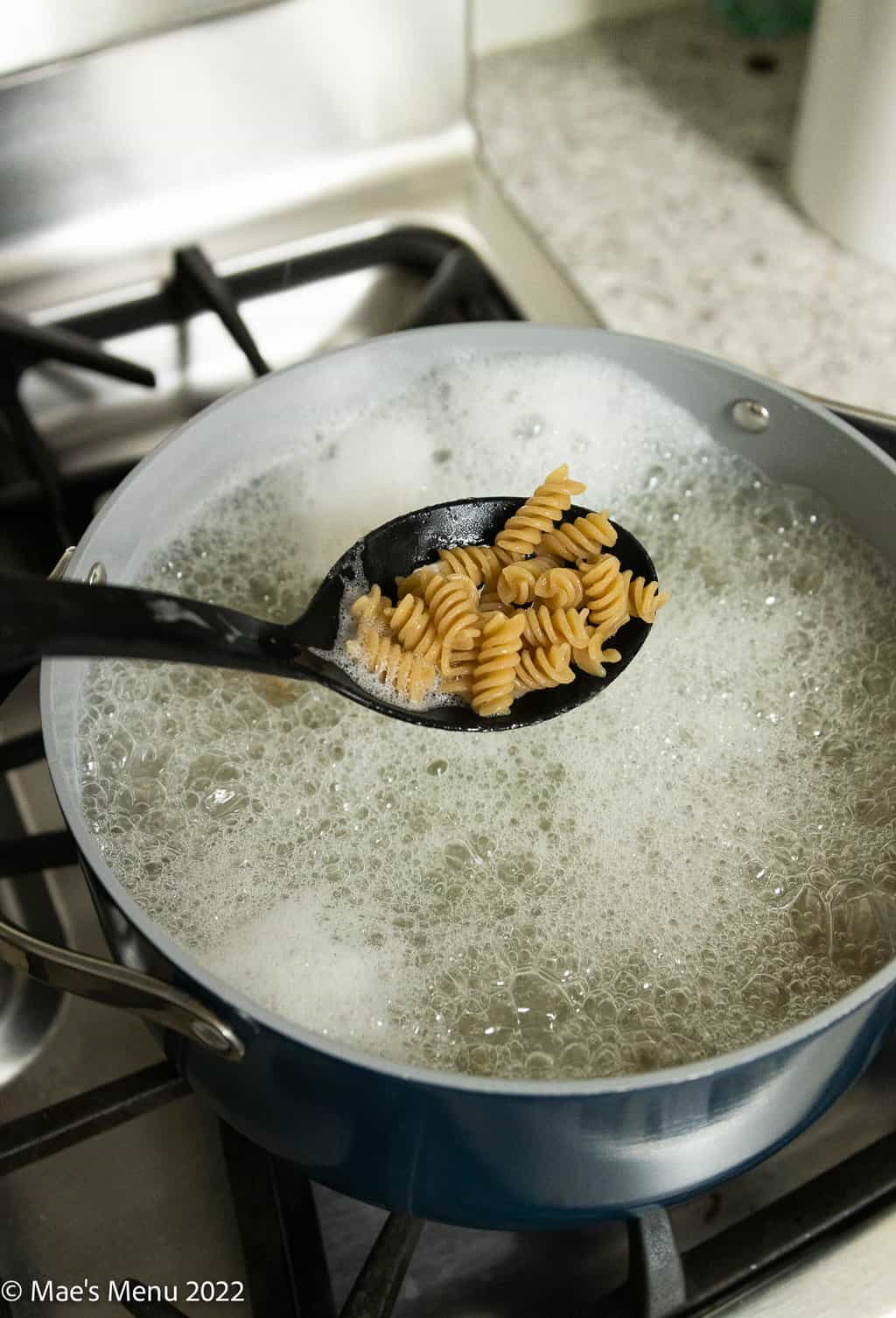 A Dutch oven boiling pasta with a spoon scooping up pasta as it cooks.