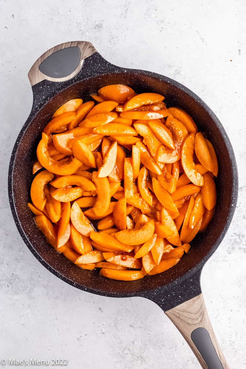 Simmered apricots in a black skillet.