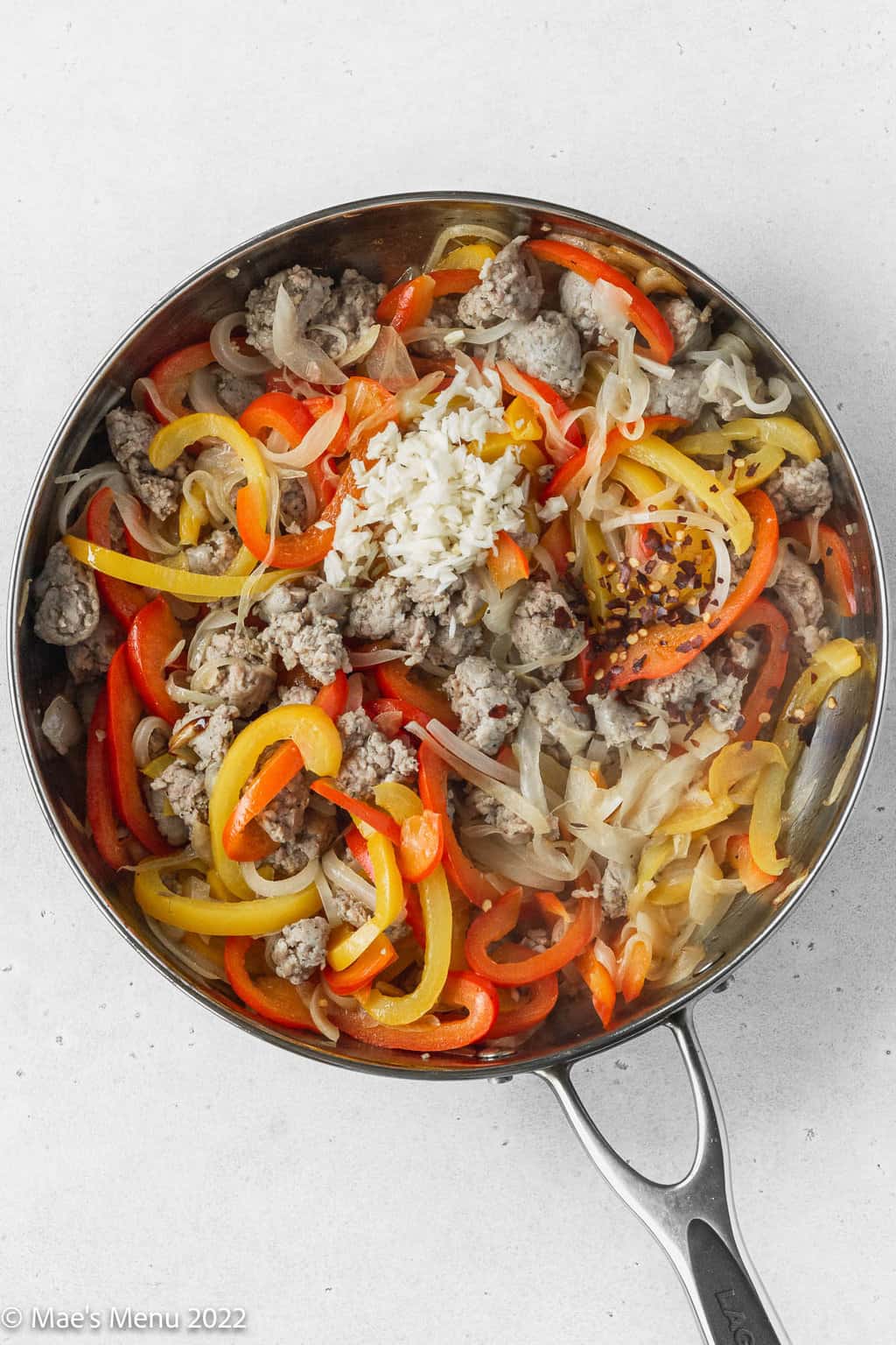 An overhead shot of a skillet with sausage, peppers, onions, red pepper, and garlic.