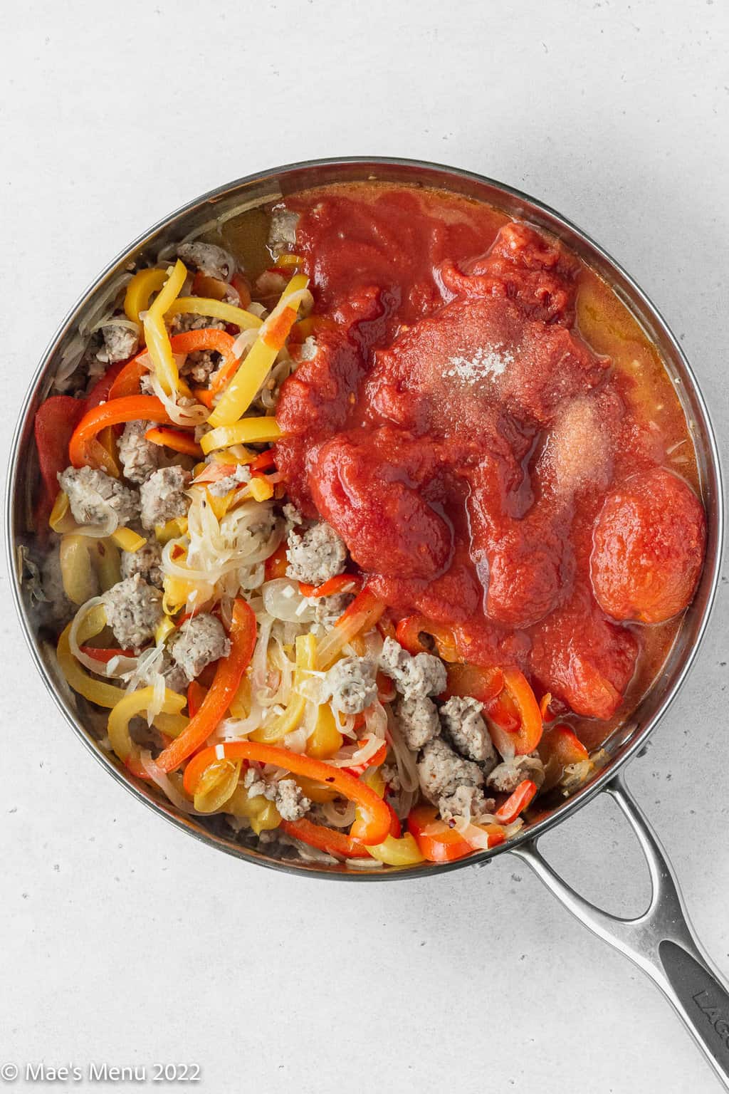 A skillet with tomatoes, salt, peppers, onion, sauce, and red pepper.