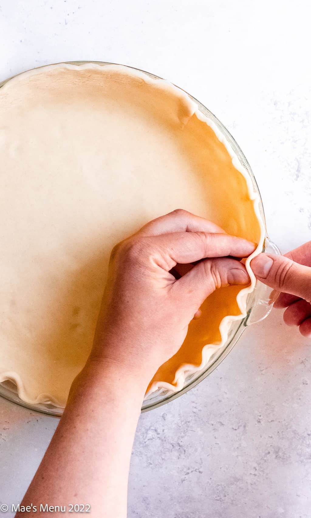 Two hands crumping pie crust in a pie plate.
