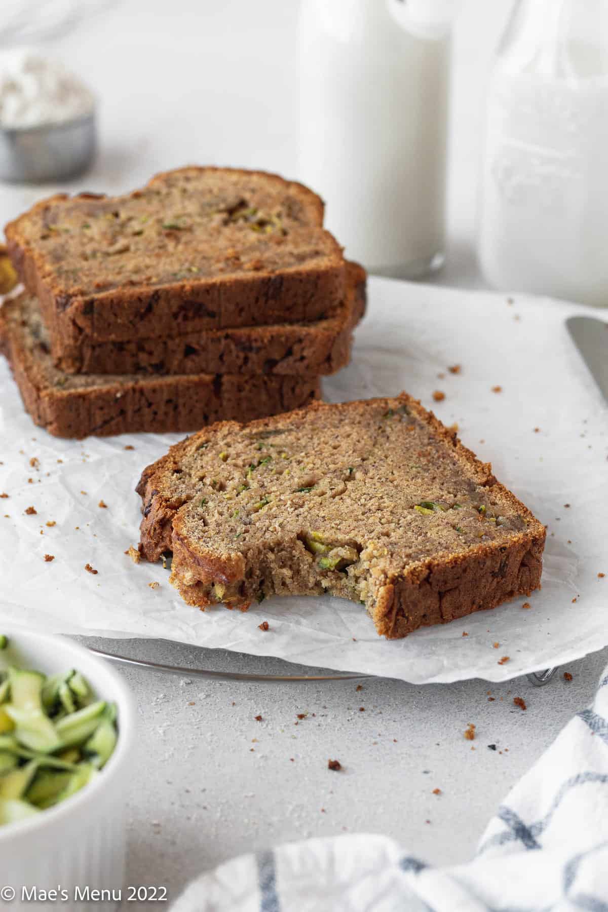 A Stack of slices of banana zucchini bread and one piece with a bite taken out of it on a white background.