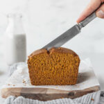 hand holding a silver knife and cutting into a fresh loaf of pumpkin bread.
