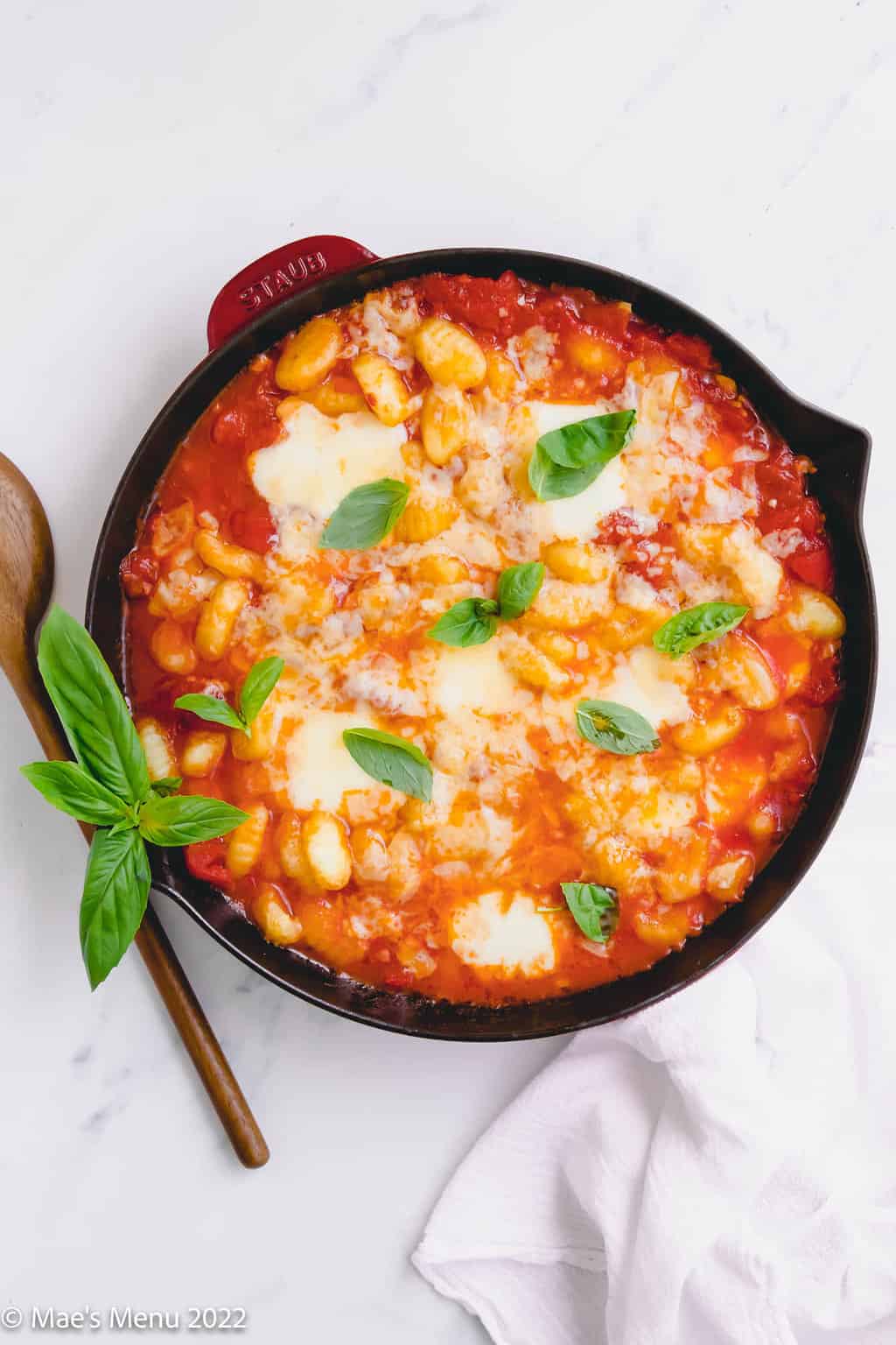 A pan of gnocchi sorrentina with basil and a wooden spoon.