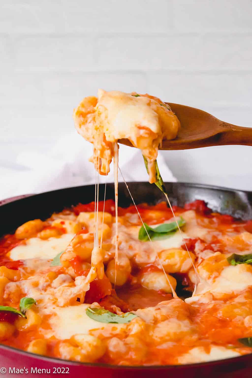 A wooden spoon taking a large scoop of cheesy gnocchi alla sorrentina out of a large pan.