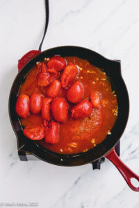 A large skillet with whole canned tomatoes and garlic.