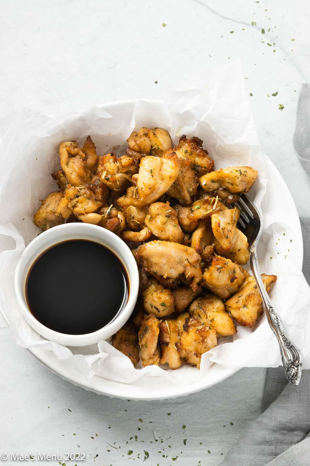 A parchment paper lined bowl of air fryer chicken bites with a small dipping dish of soy sauce.