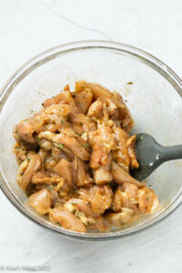 Chicken pieces stirred with seasonings in a glass mixing bowl.