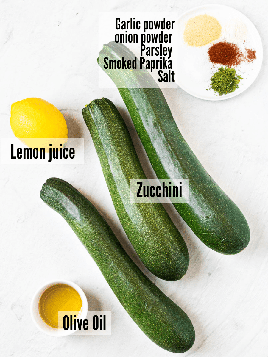 All of the ingredients for air fryer zucchini: zucchini, lemon juice, olive oil, garlic powder, onion powder, parsley, smoked paprika, salt.
