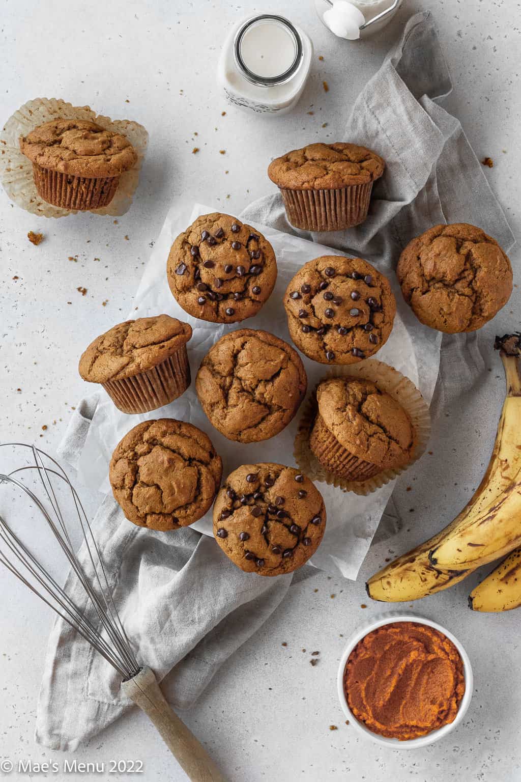 An overhead shot of banana pumpkin muffins on the counter with bananas, milk, a whisk, and pumpkin puree.