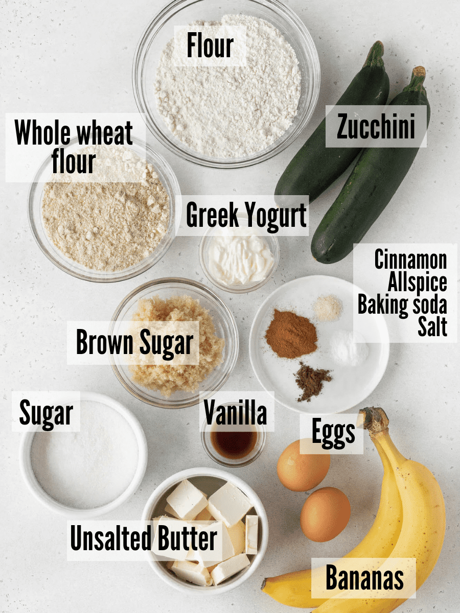 All of the ingredients for banana zucchini bread: all purpose flour, whole wheat flour, zucchini, greek yogurt, cinnamon, allspice, baking soda, salt, brown sugar, vanilla, unsalted butter, eggs, bananas, and sugar.