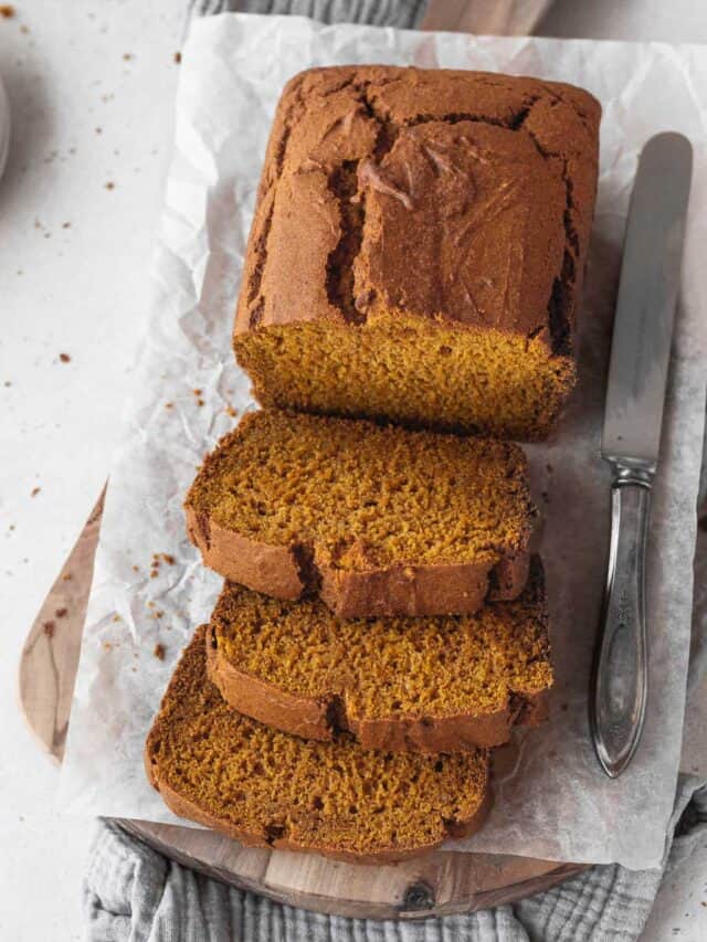 angled overhead shot of loaf of gluten free pumpkin bread with 3 slices made from the front half and a silver knife on the side.