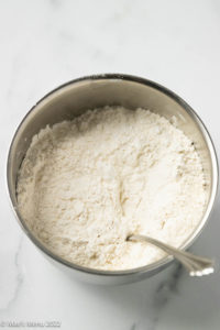 An angled shot of a small silver bowl of flour with corn starch, baking soda, and salt.