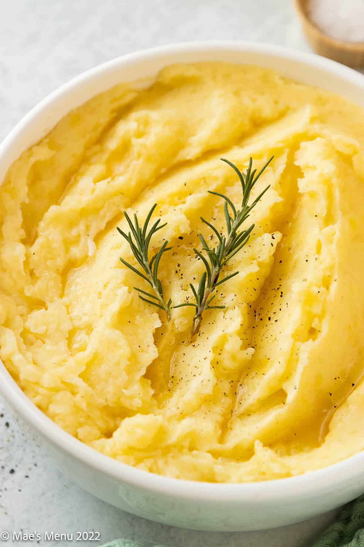 A white bowl of dairy free mashed potatoes with two sprigs of rosemary on top.