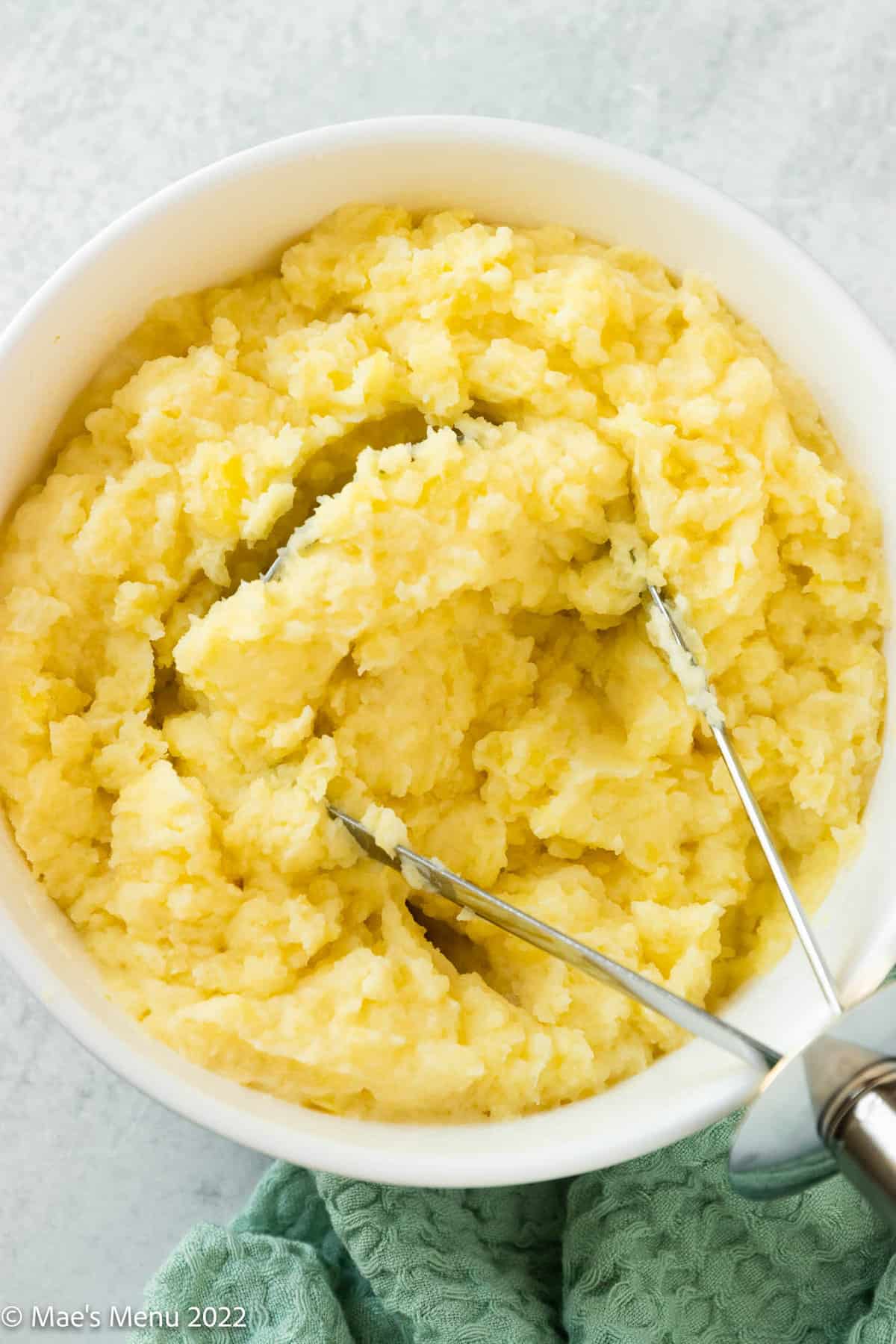 A white bowl of dairy free mashed potatoes with a potato masher.