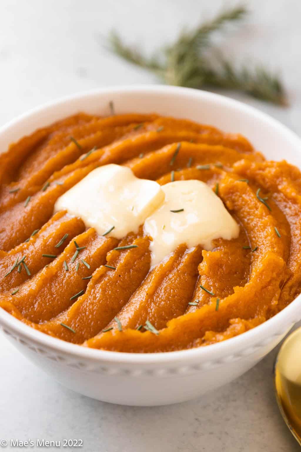 An up-close side shot of a large bowl of whipped sweet potatoes with pats of melted butter.
