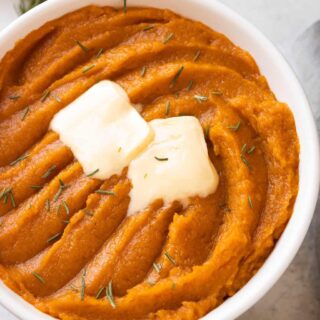 A white serving bowl of whipped sweet potatoes with butter.