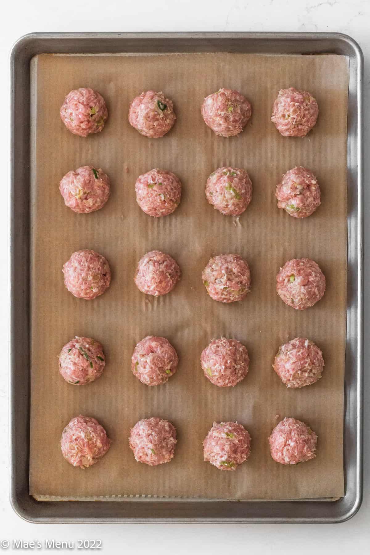 unbaked asian pork meatballs on a parchment-lined baking sheet.
