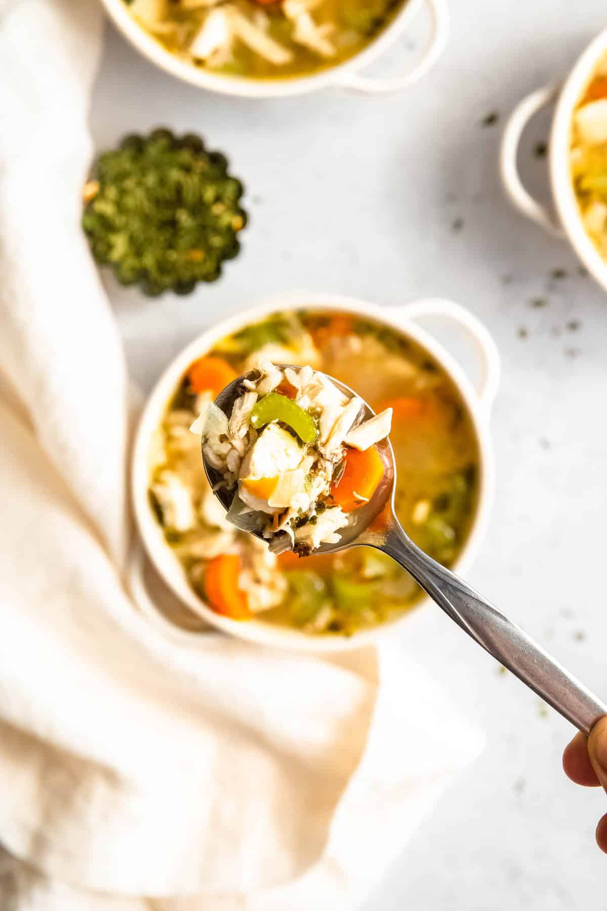 Holding a spoonful of turkey rice soup over the bowls of soup.
