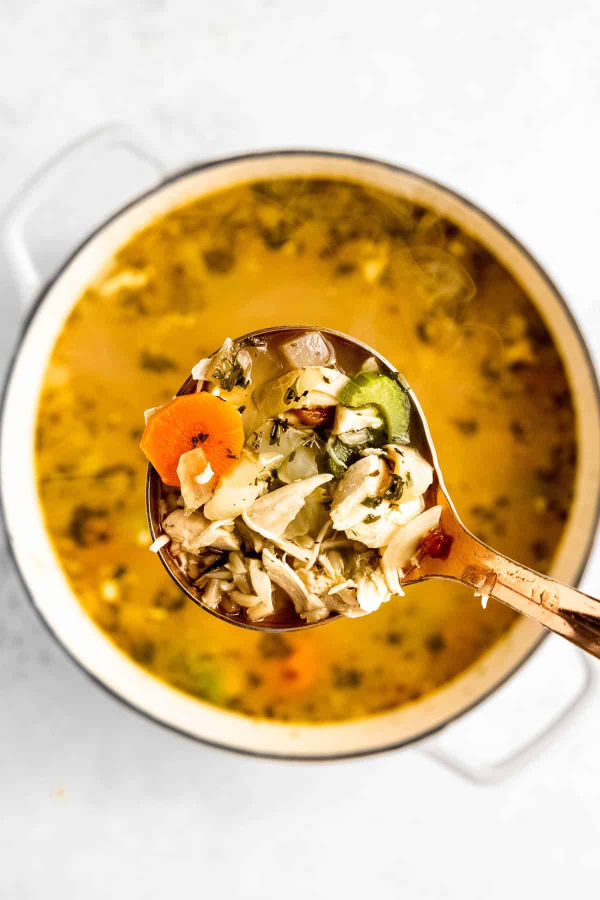 A large ladle of turkey rice soup over the pot of soup.