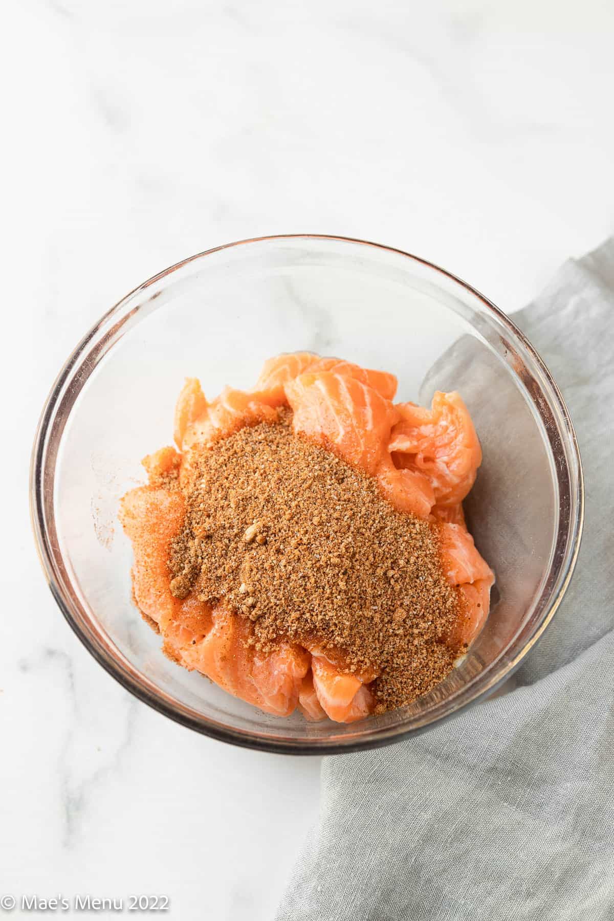 A glass bowl of slices of salmon with brown sugar seasoning on top.