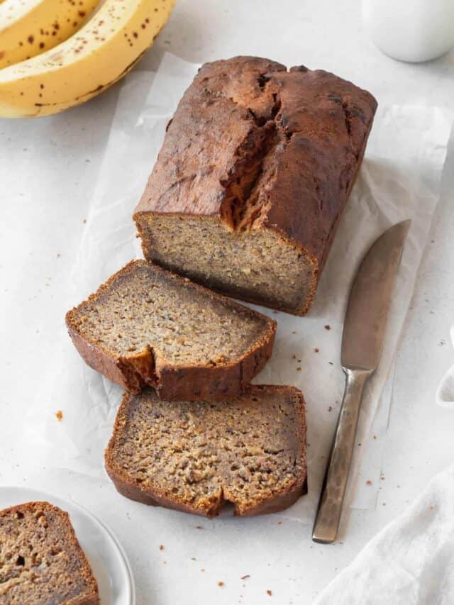 Sliced gluten free dairy free banana bread with a knife on a white background.