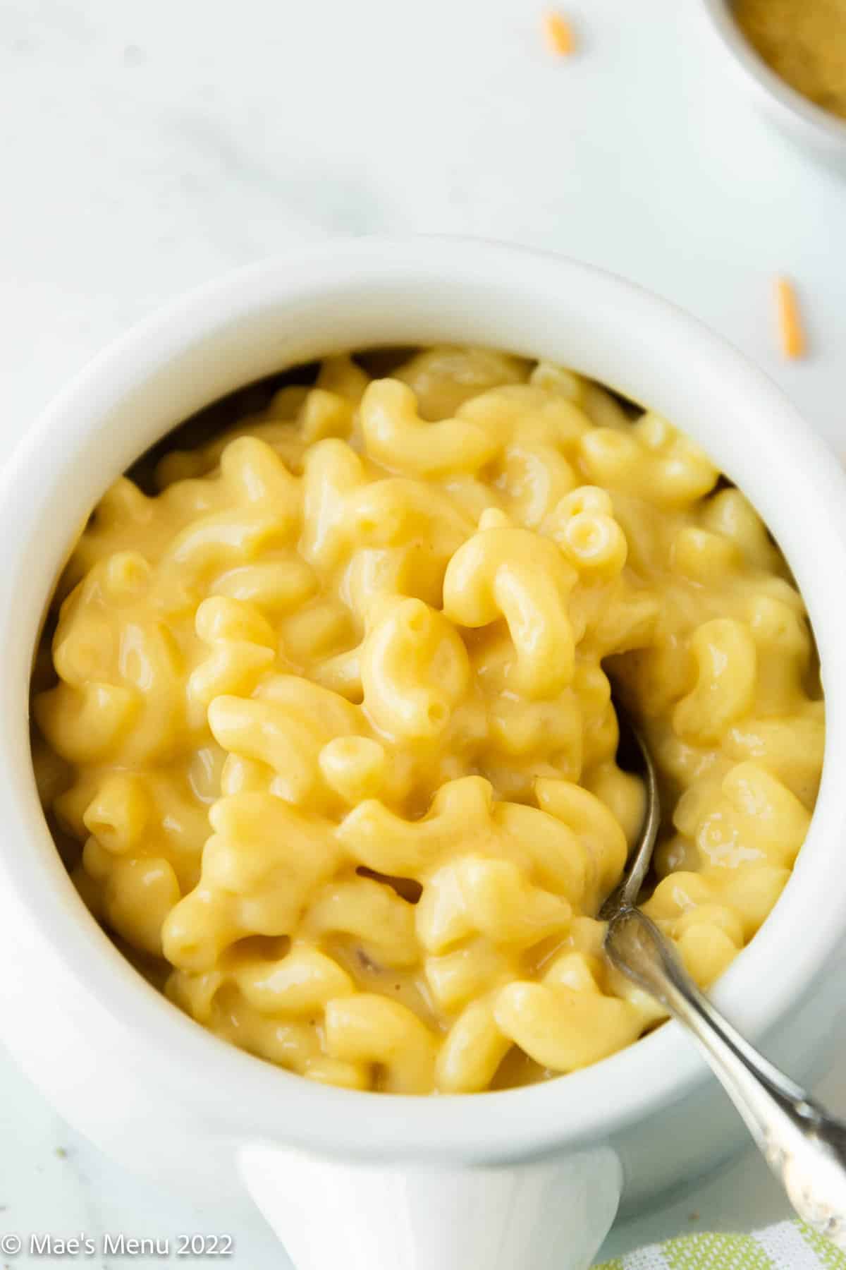 small white crock of lactose free macaroni and cheese with a silver spoon.