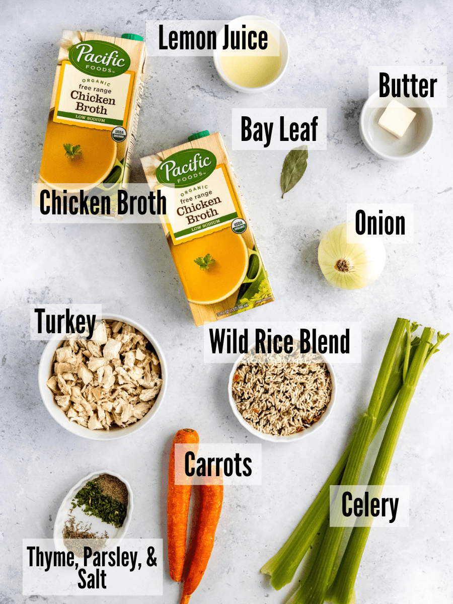 The ingredients for turkey rice soup: chicken broth, lemon juice, butter, onion, bay leaves, celery, rice, carrots, turkey, and dried spices.