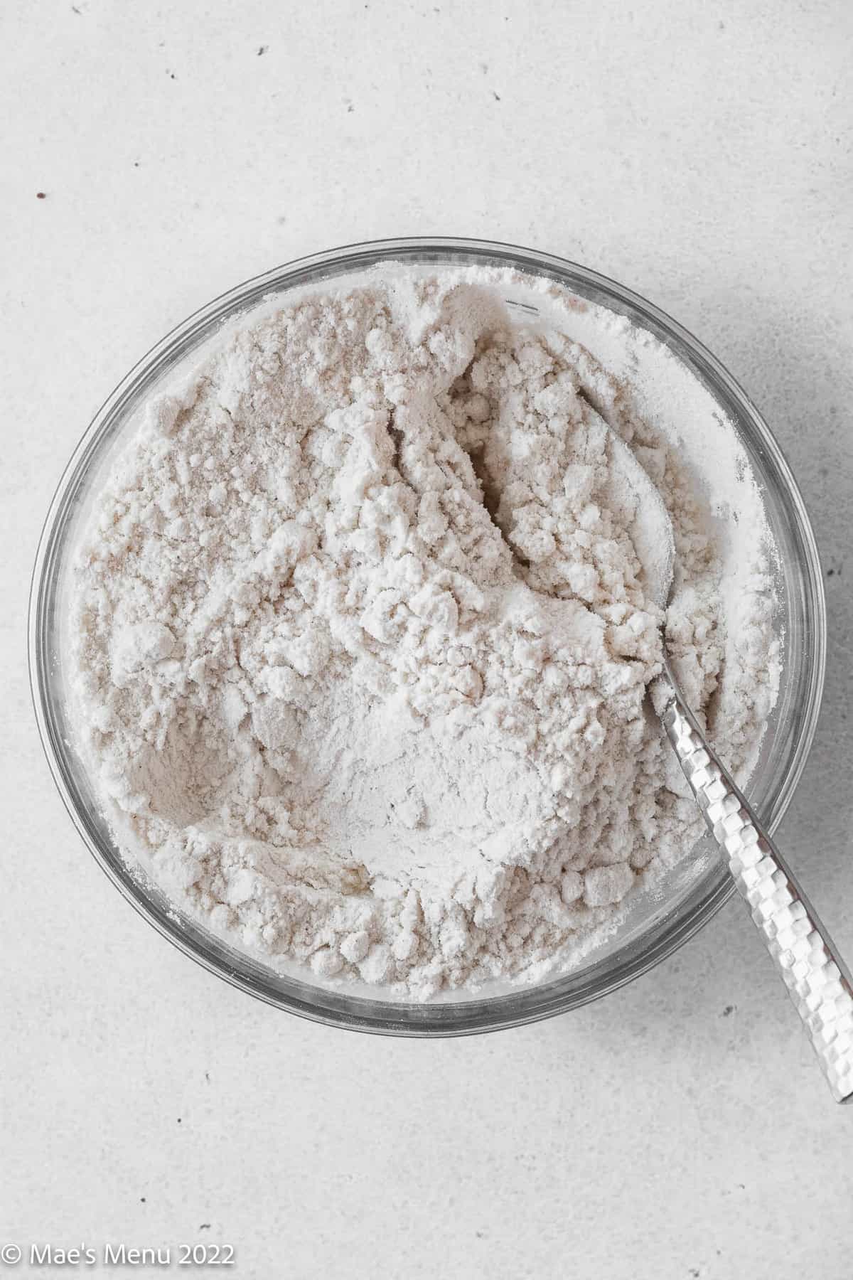 A glass mixing bowl of flour with a whisk.