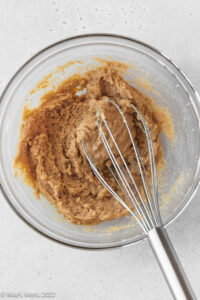 A glass mixing bowl of peanut butter, butter, and sugars.