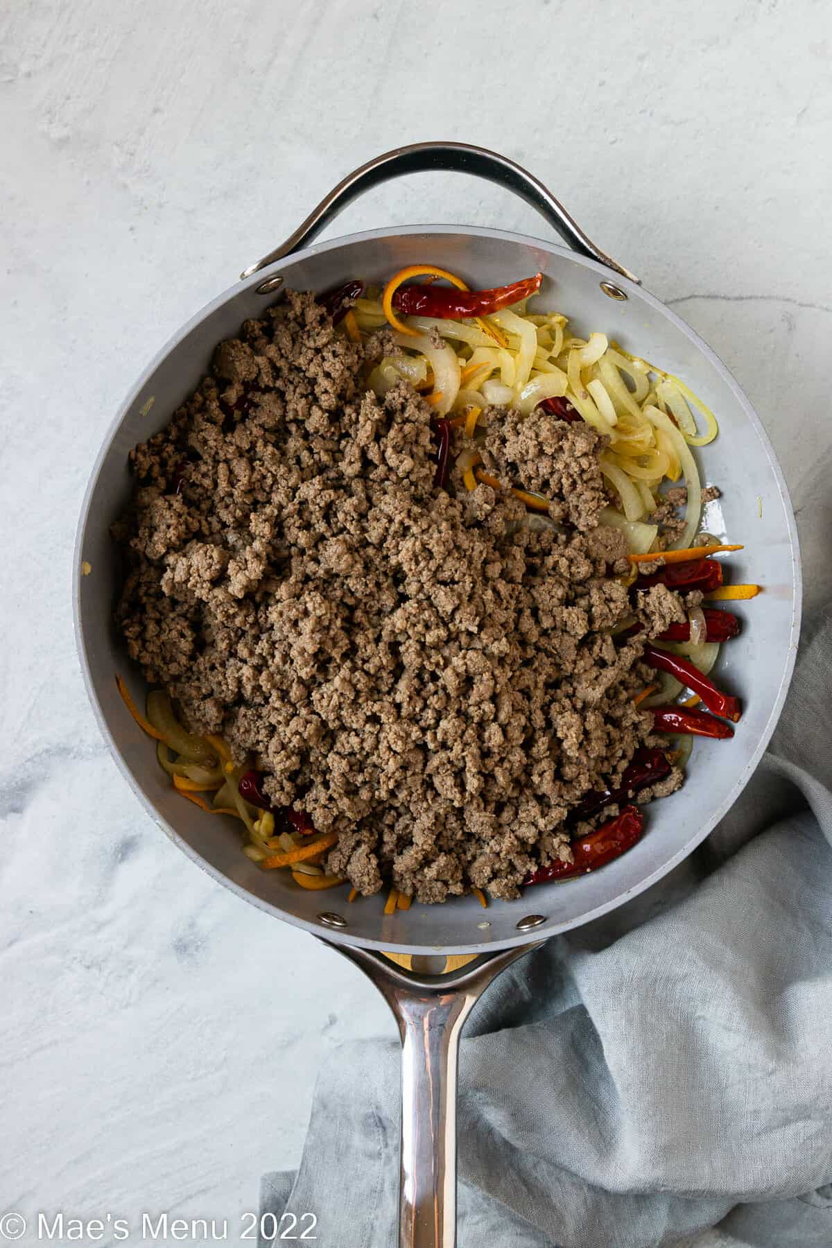 A skillet with onions, chiles, orange juice, and ground beef.