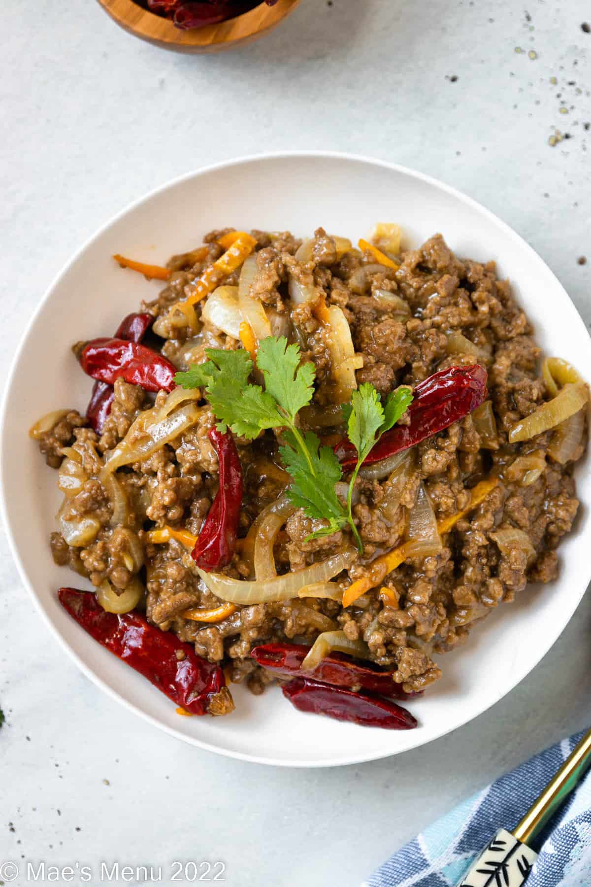 A white erving bowl of ground beef stir fry with cilantro.
