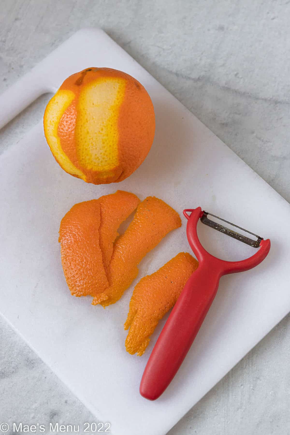 An orange with 4 pieces of zest peeled off of it.