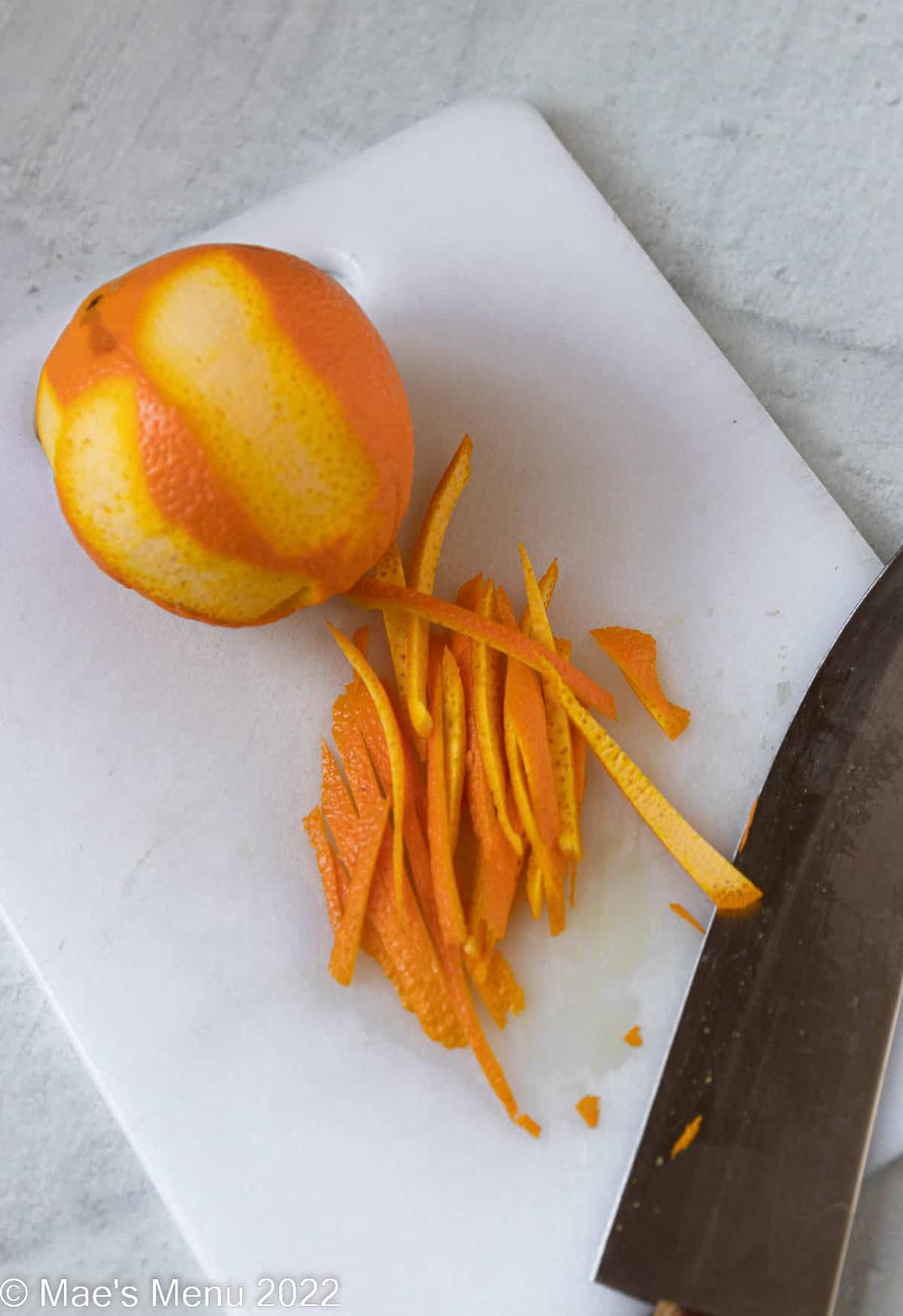 Sliced orange zest on a cutting board with a knife.