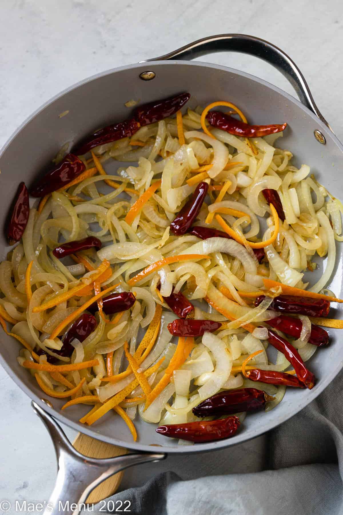 A large skillet of onions, garlic, Sichuan chiles, and orange zest.
