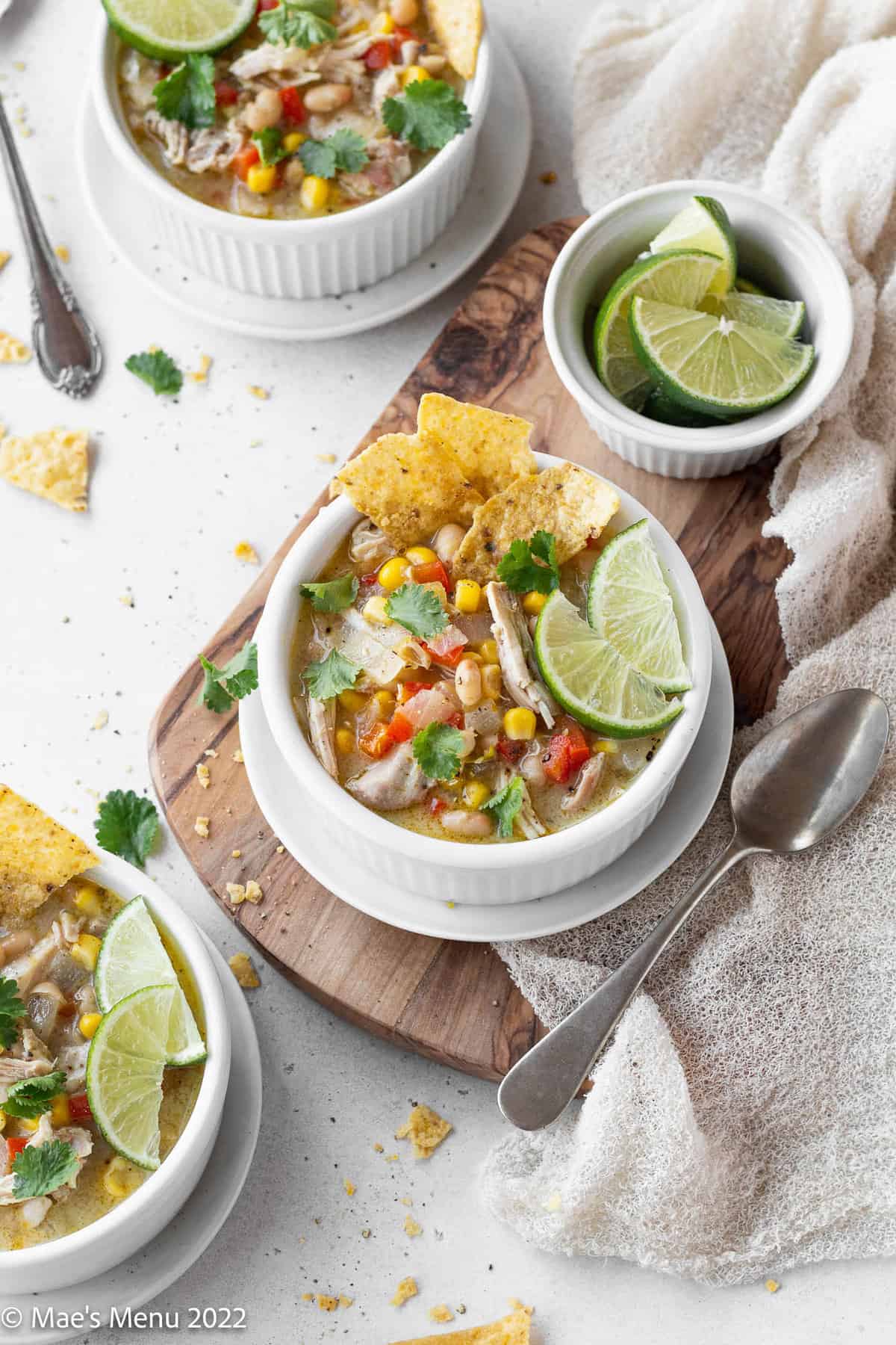 Bowls of creamy white chicken tortilla soup with limes, tortilla chips, and spoons.