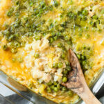 A clear glass pan of cheesy tuna rice casserole with a large serving spoon in it.