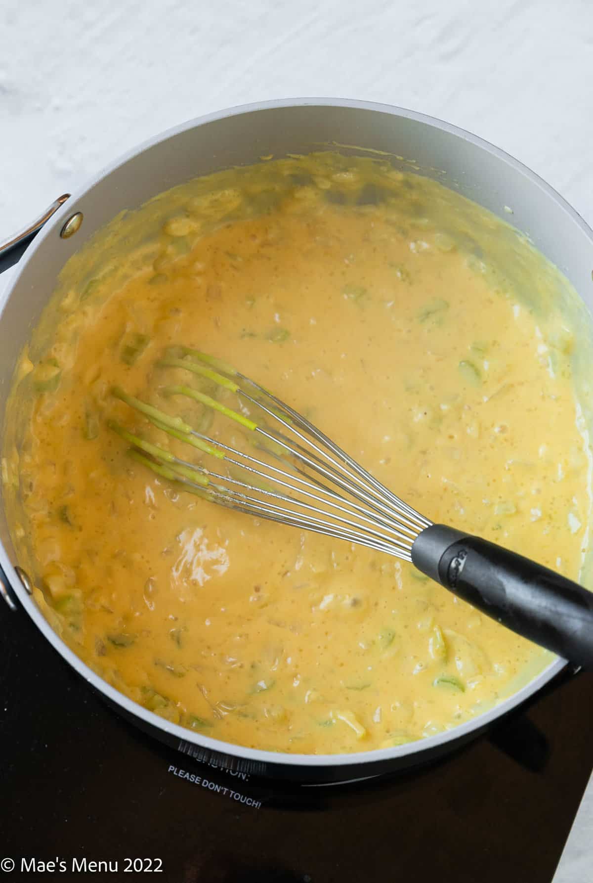 A large pot of cheese sauce with a whisk.