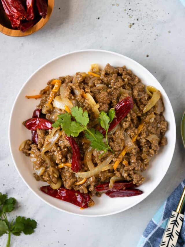 A serving bowl of ground beef stir-fry next to a small dish of sichuan chiles.