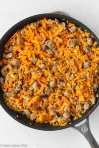 A skillet with cooked shredded sweet potatoes and breakfast sausage.