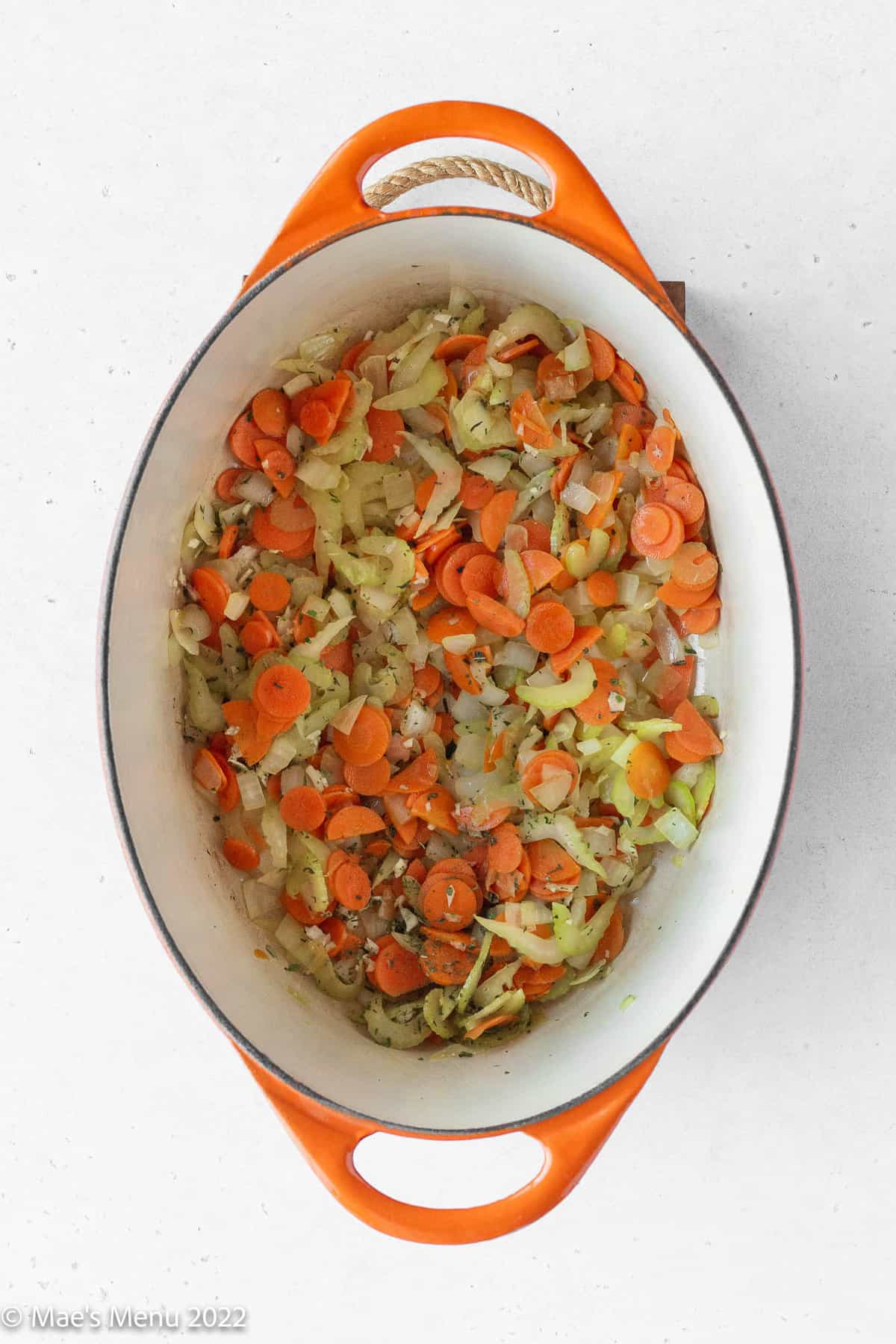 sautéed mirepoix in an orange dutch oven with garlic and herbs added.