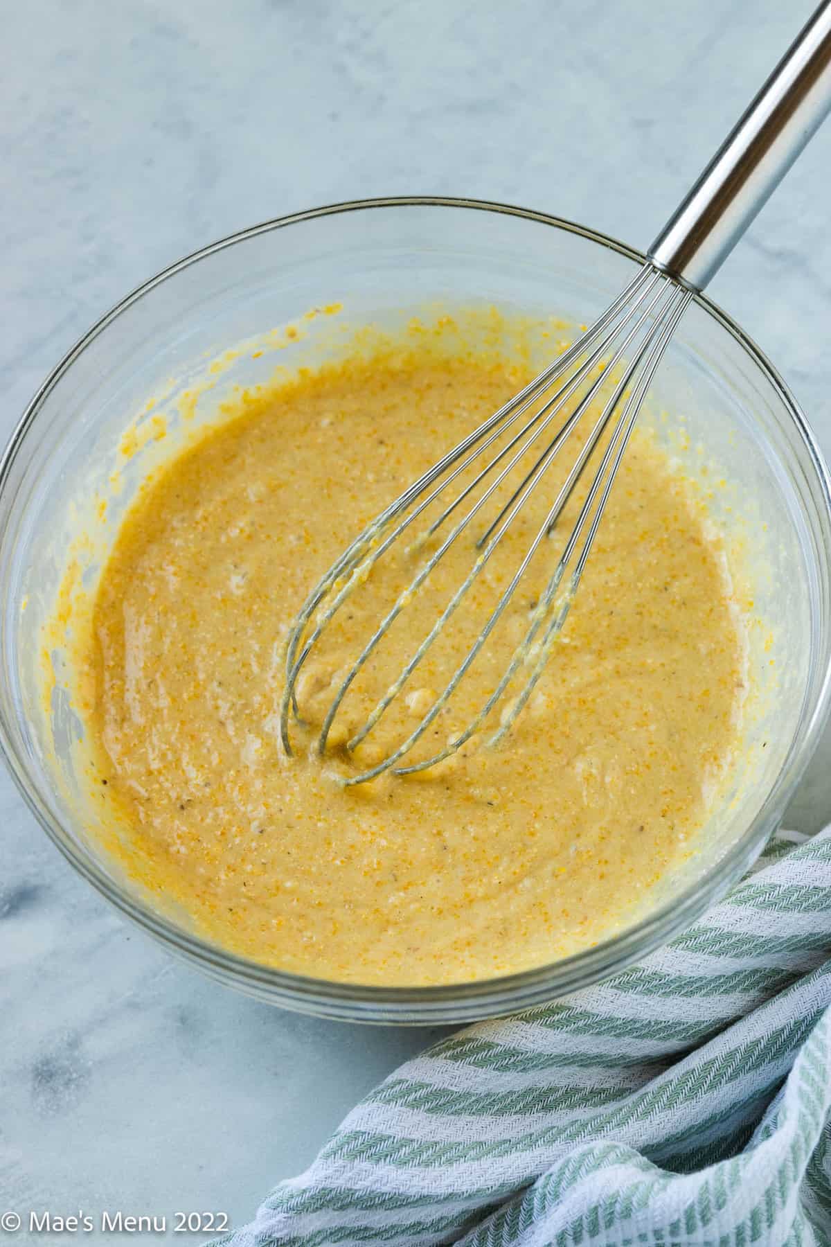 A glass bowl of dairy-free cornbread batter with a whisk in it.