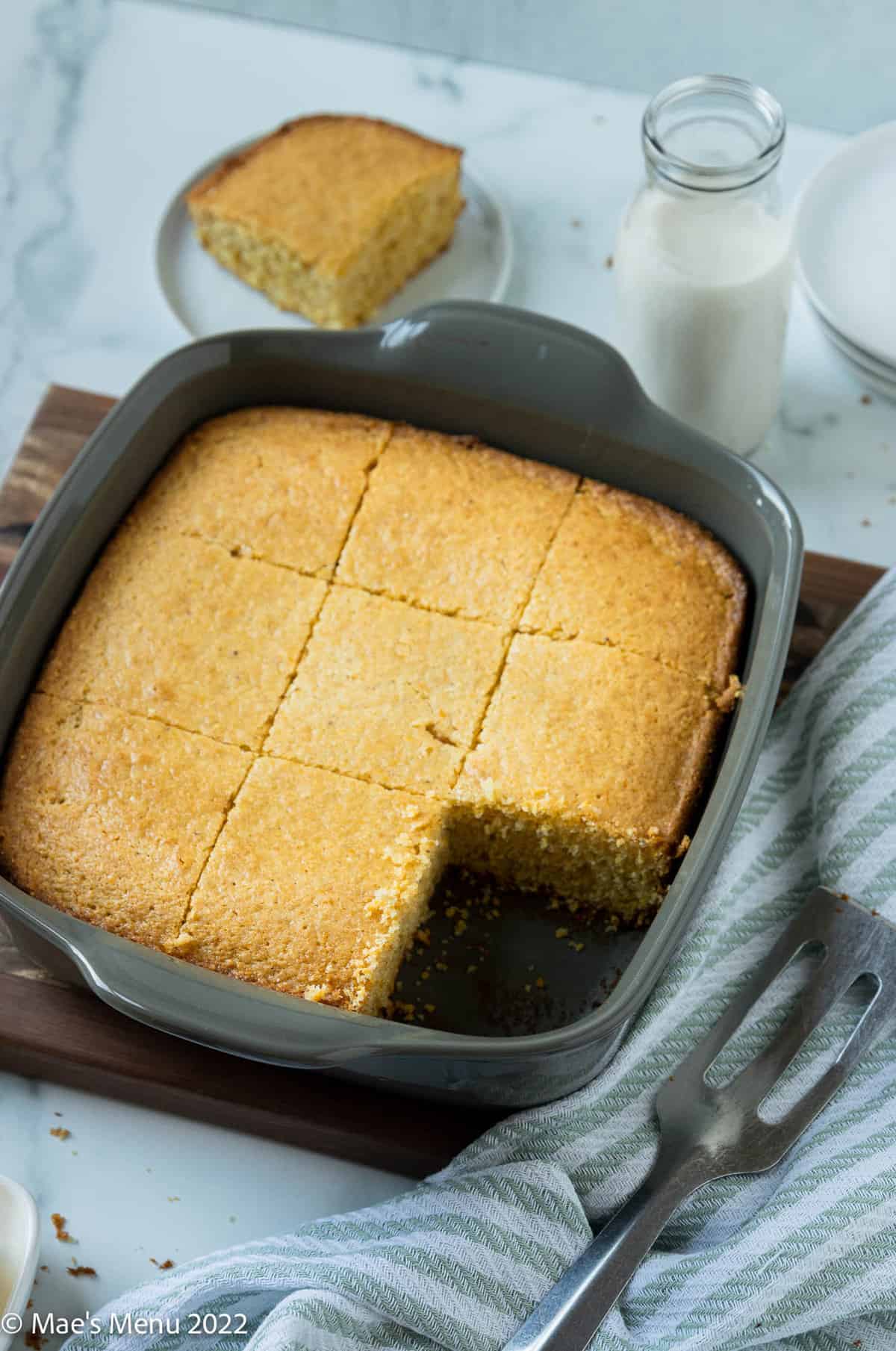 Sliced loaf of cornbread made without milk in a grey pan with a slice taken out of it.