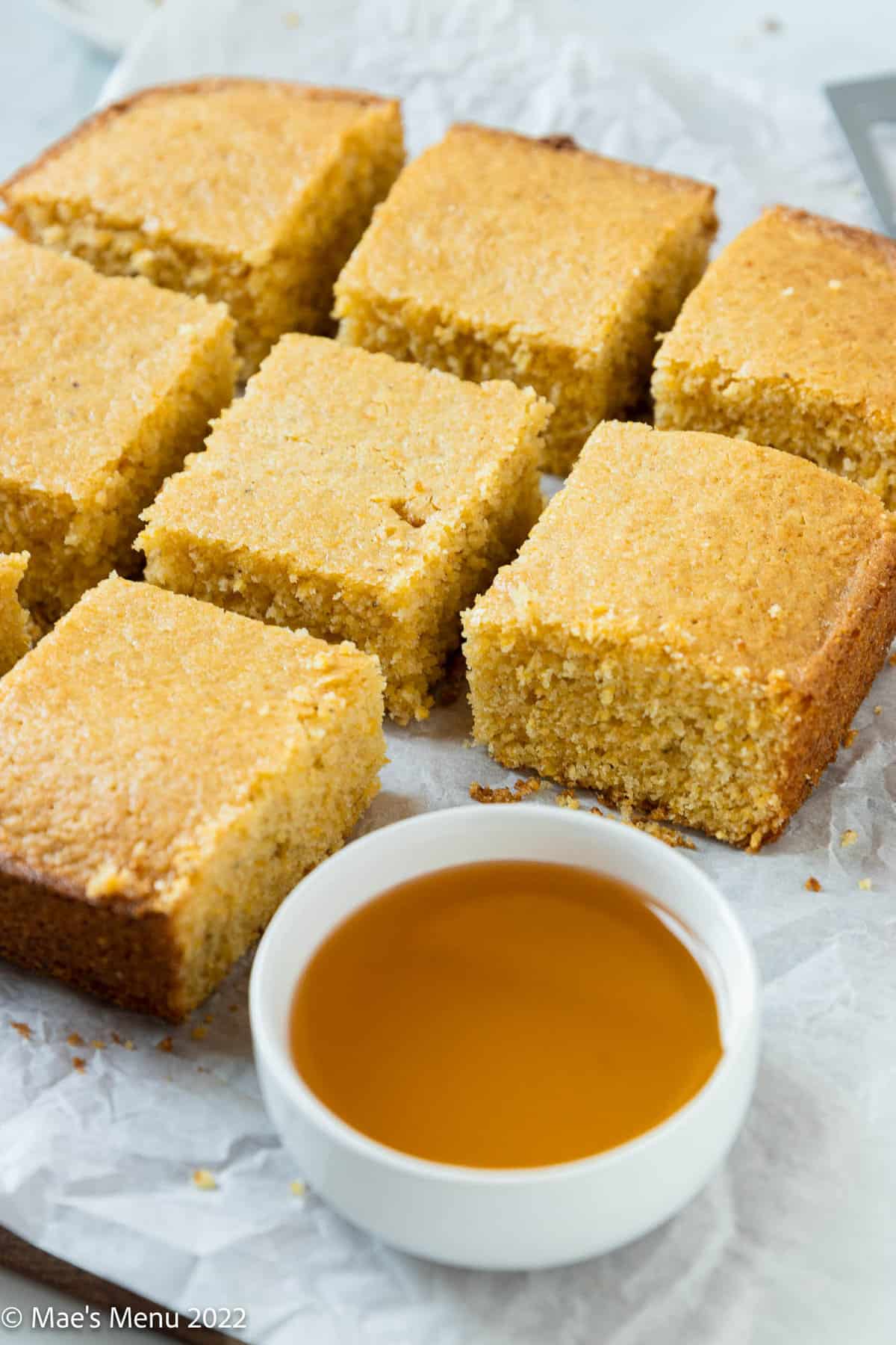 Sliced cornbread on parchment paper with a cup of honey.