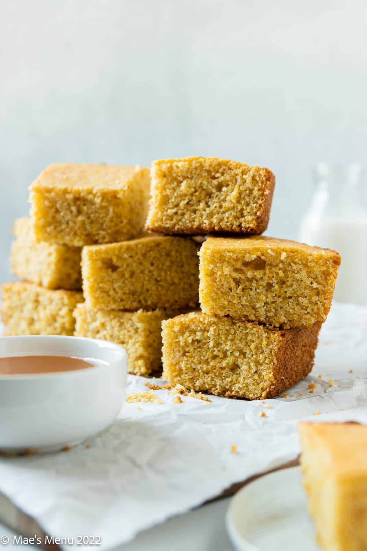 A stack of dairy-free cornbread on parchment paper with a jar of milk in the background.