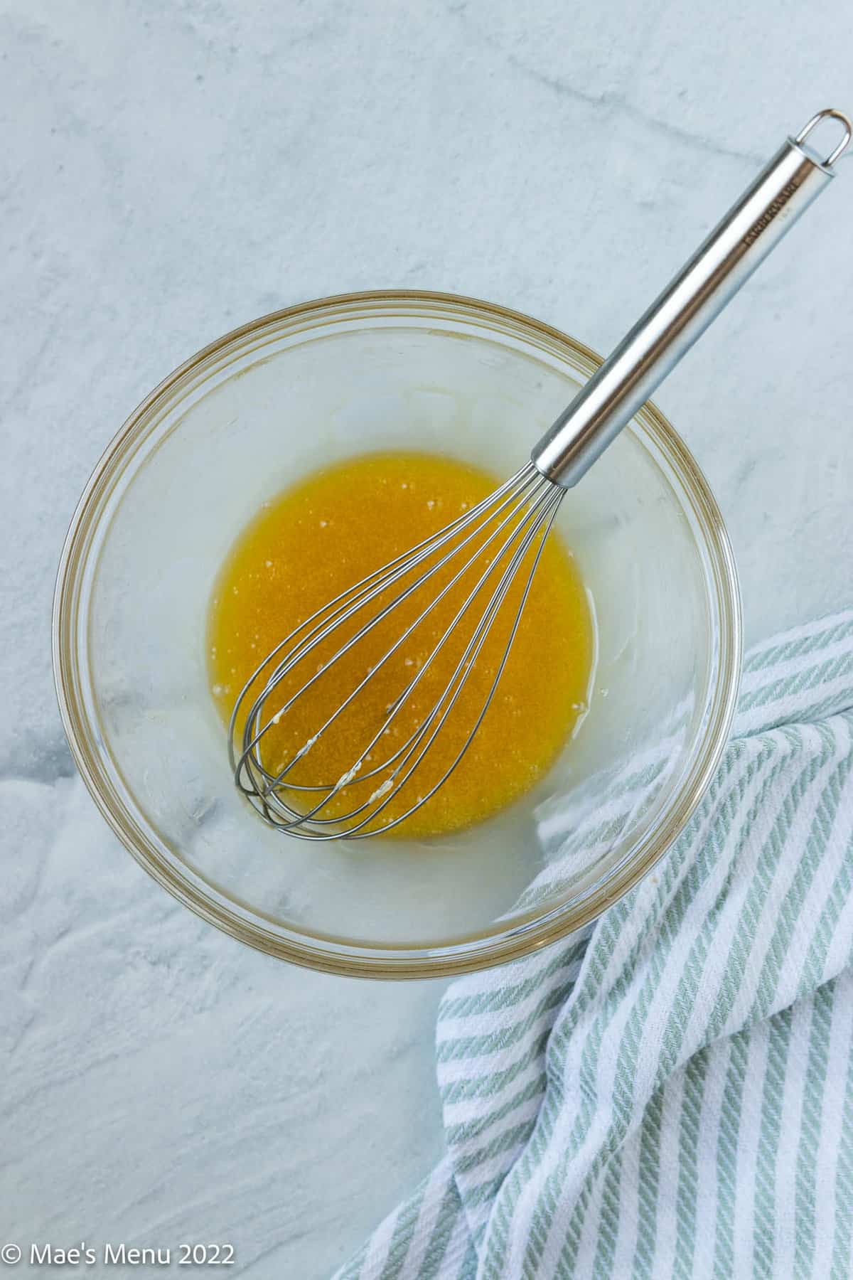 A glass mixing bowl of melted honey and butter with a whisk.